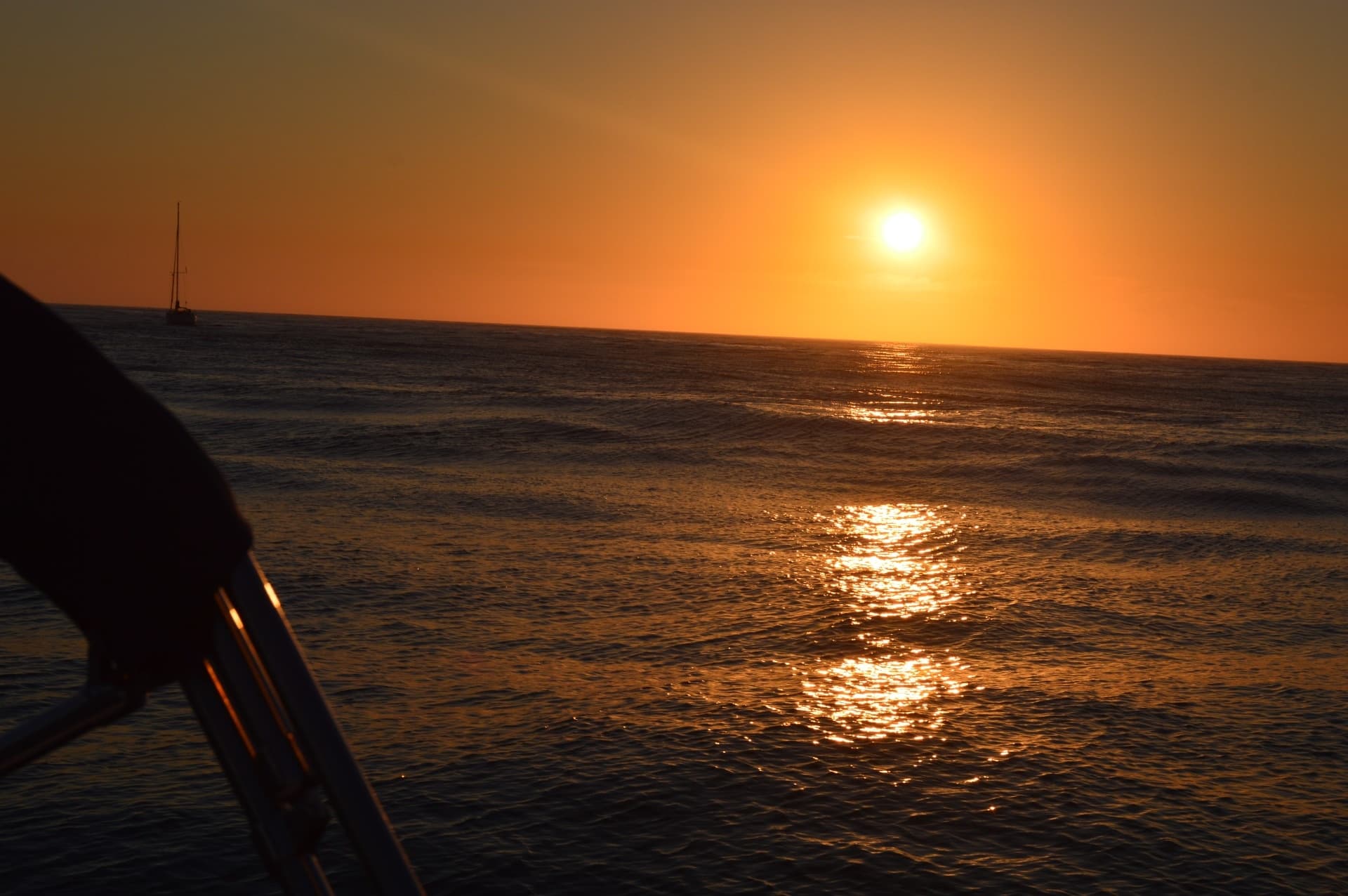 Sunset viewed from boat with sun reflection and distant sail