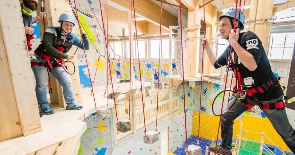 Participants navigating indoor climbing ropes course with instructor