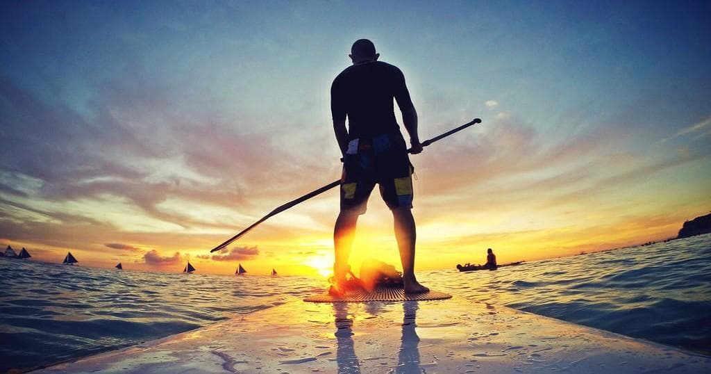 Stand-up paddleboarder silhouetted at ocean sunset
