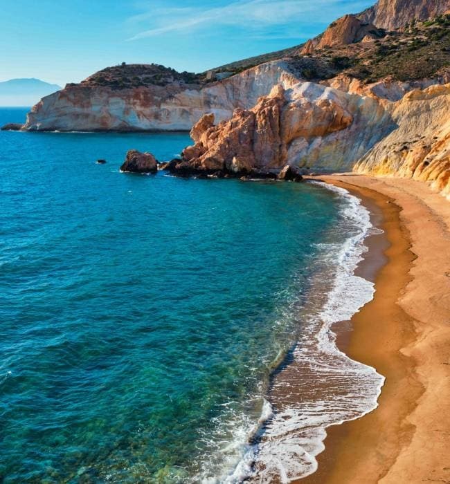 Sandy coastal shoreline with waves and rocky headland, Greece