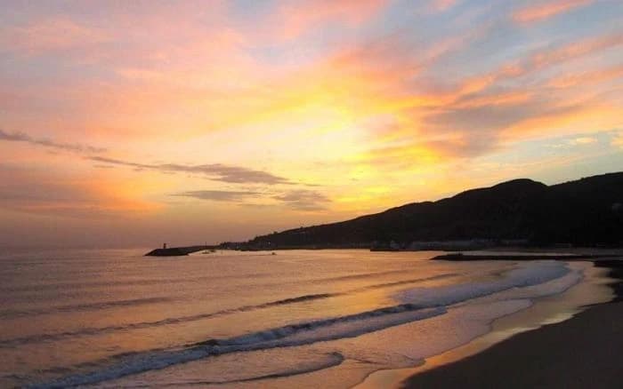 Sunset over empty sandy beach with waves ideal for scenic strolls