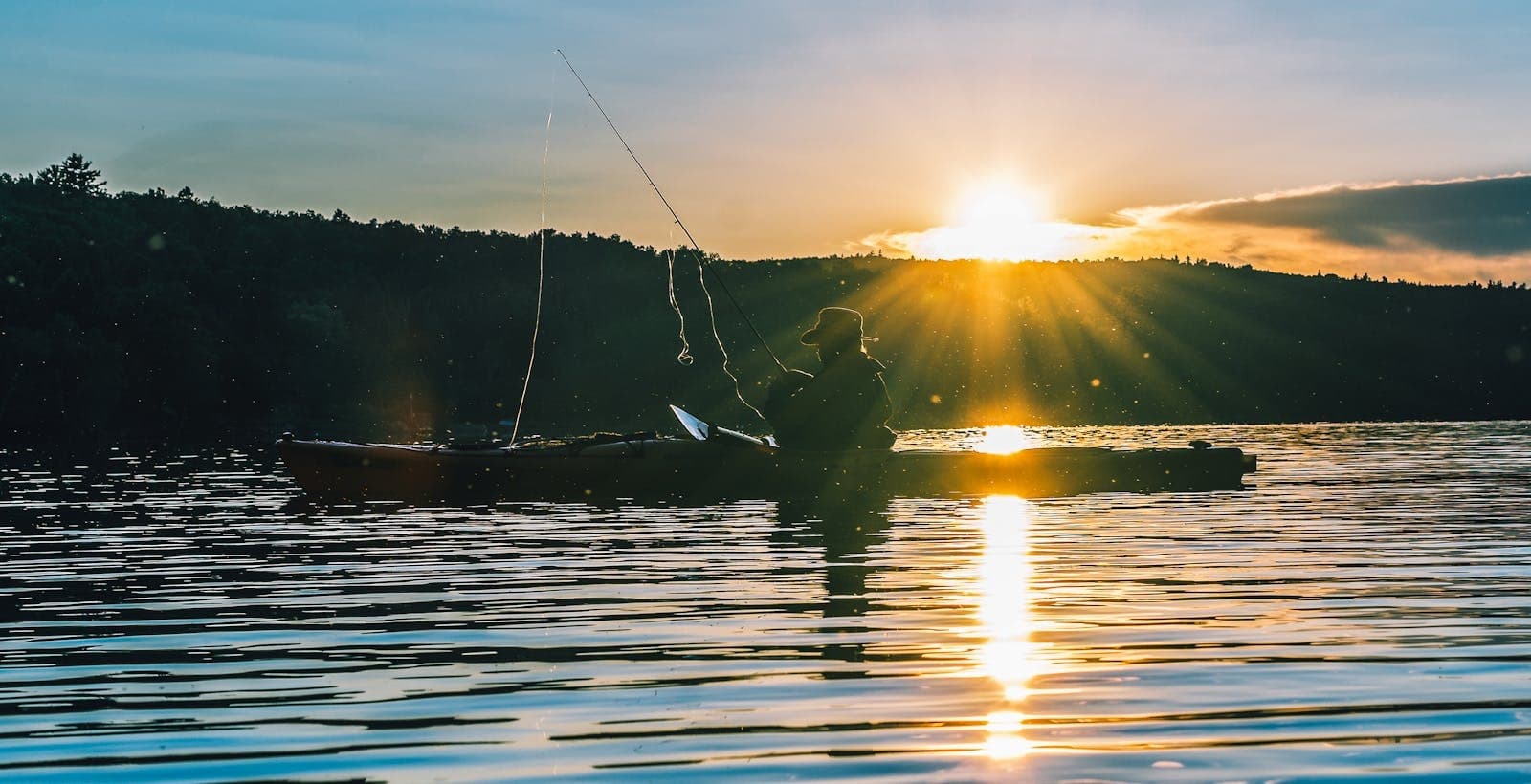 Fly-fisher casting at sunset from boat on tranquil lake