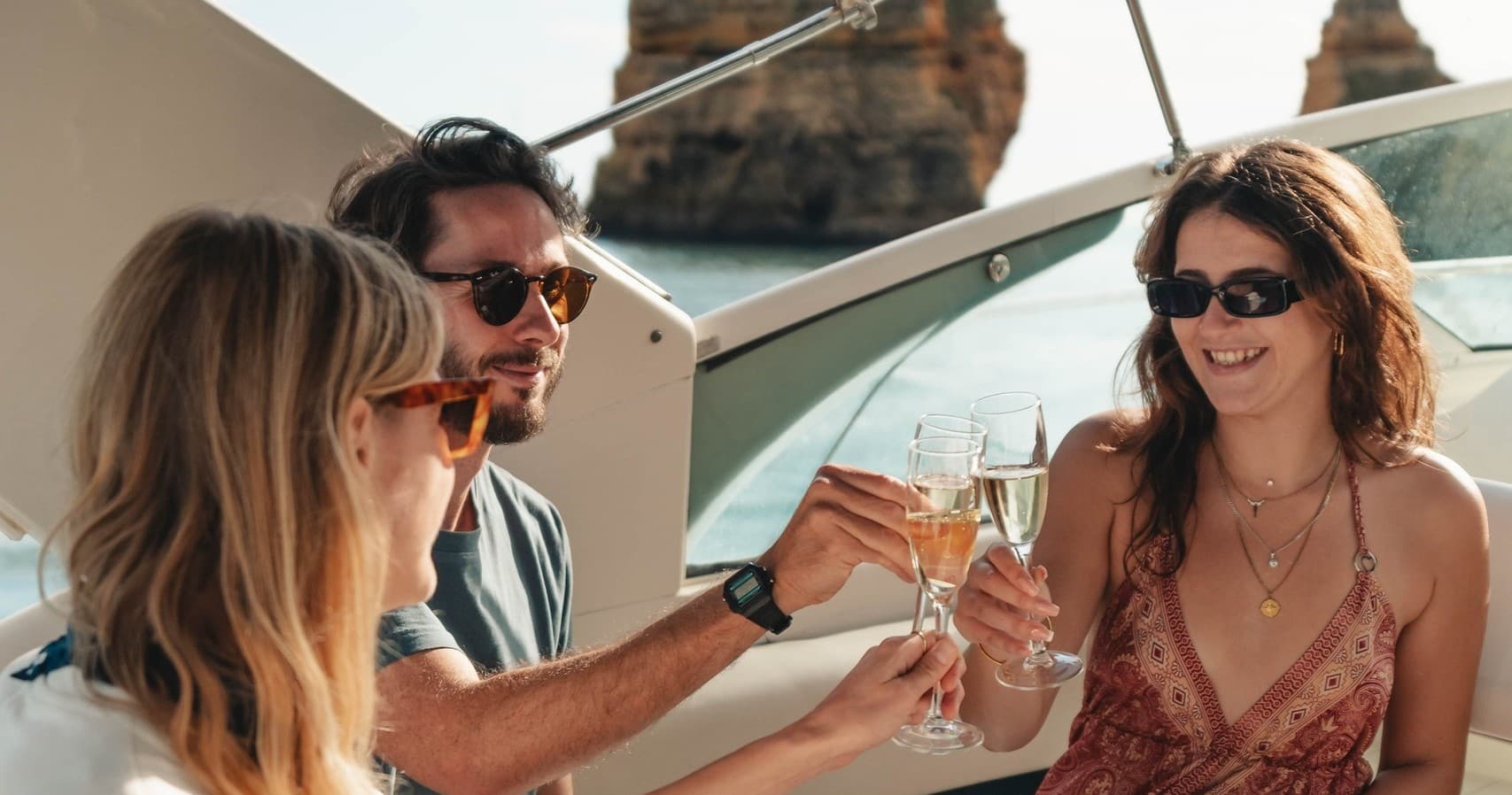 Friends toasting with drinks on yacht near rocky coastline