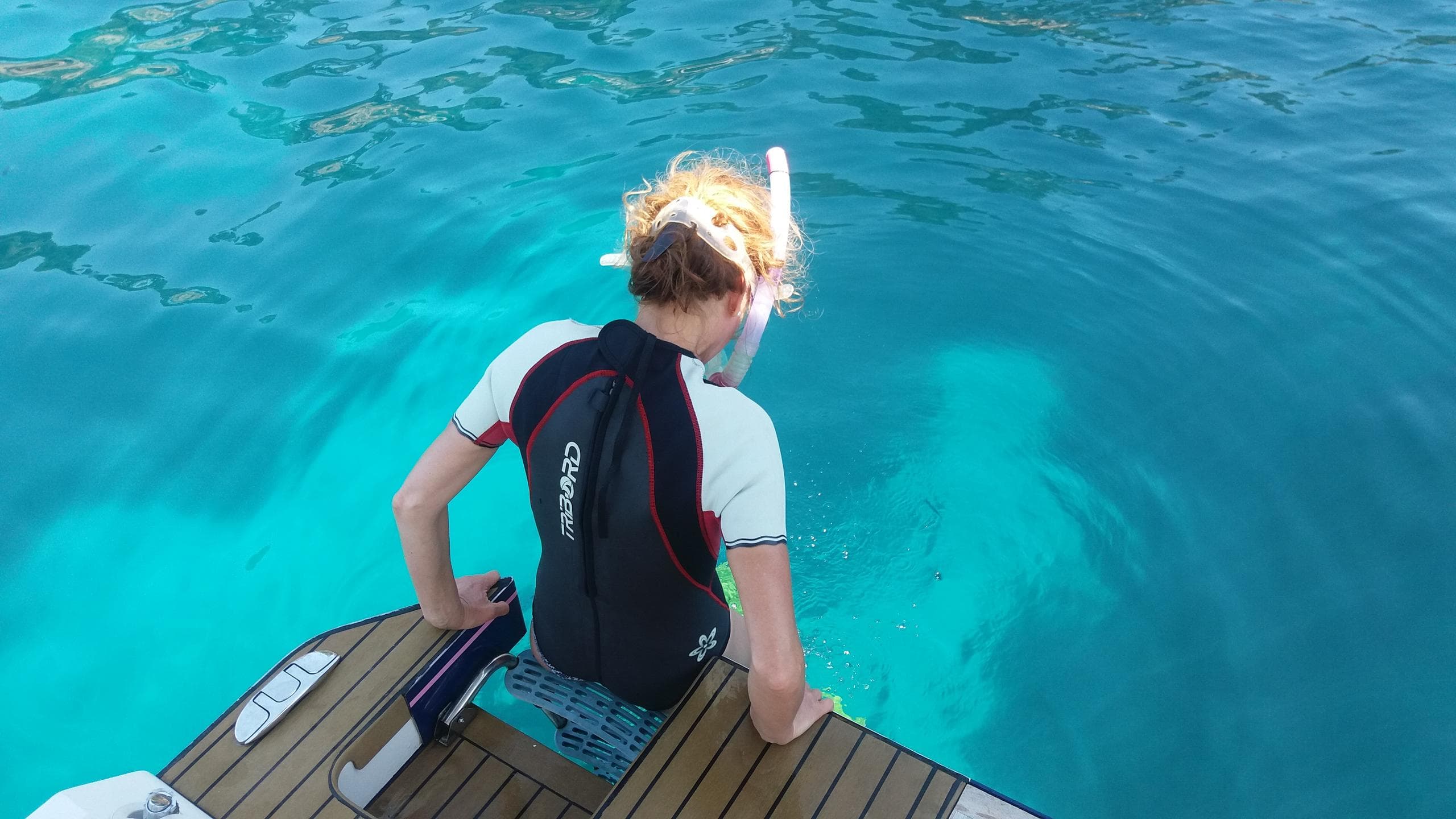 Child climbing boat ladder into bright Mediterranean blue water