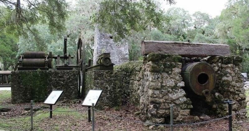 Historic coastal sugar mill ruins with tour signage in shaded forest