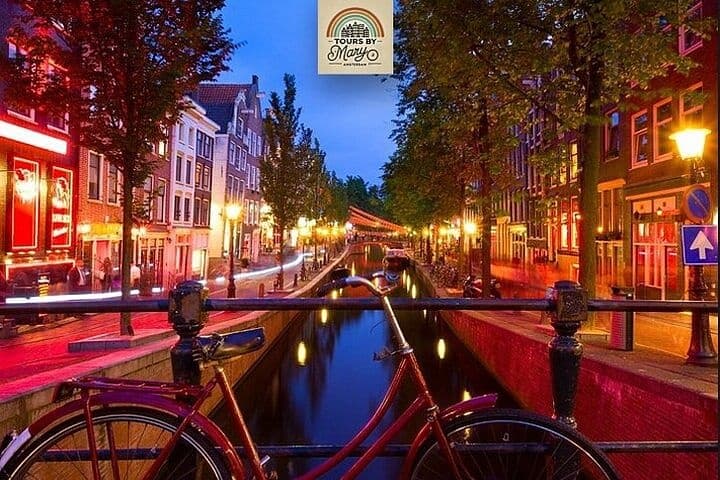Illuminated Amsterdam canal at dusk with bicycles on bridge
