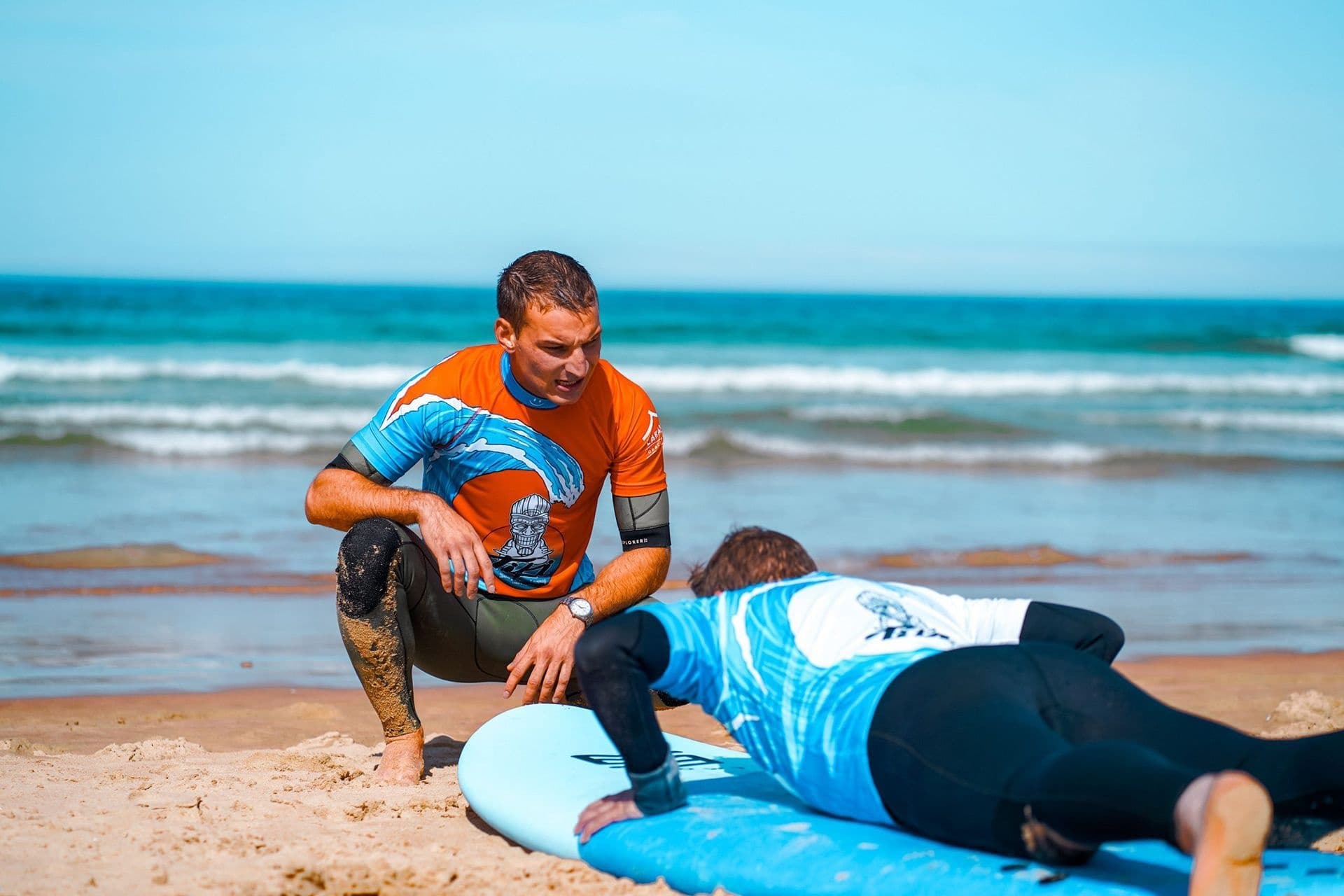 Surf instructor coaching student on beachboard during lesson