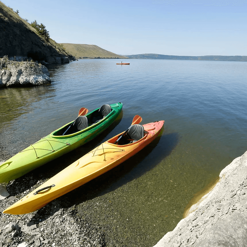 Two colorful kayaks pulled on pebble beach beside calm lake