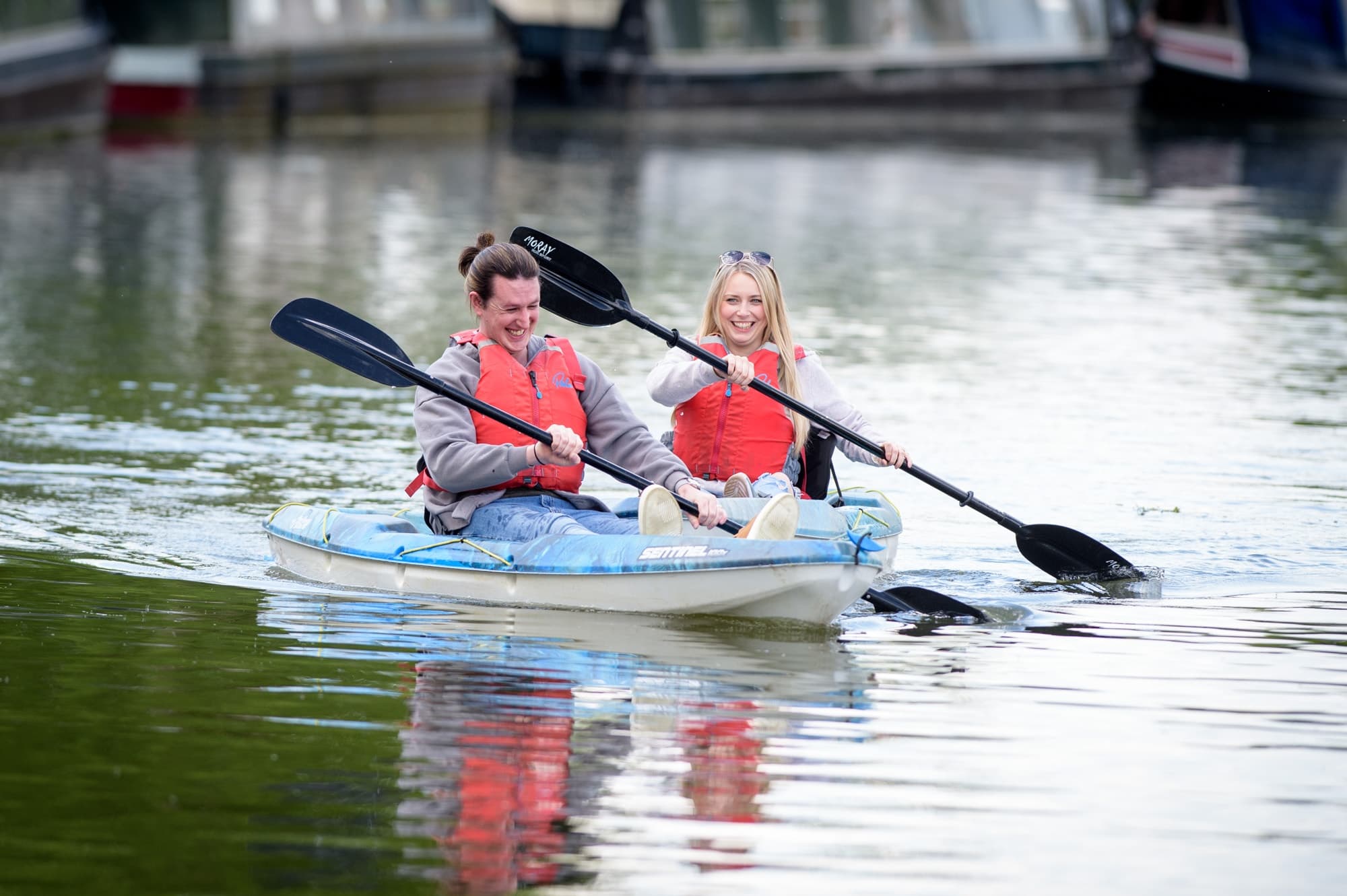 Couple kayaking on serene river with boat reflections