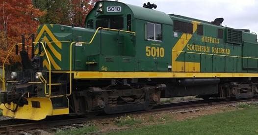 Green diesel locomotive passing autumn parkland on scenic rail tour