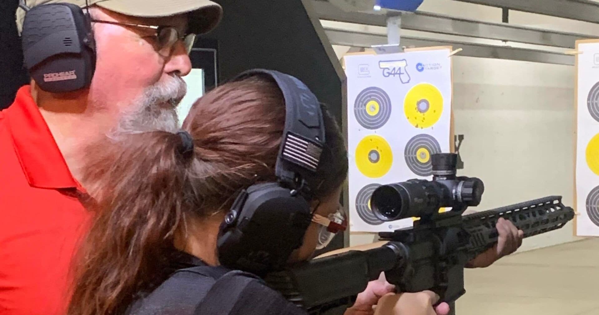 Instructor coaching woman firing rifle at indoor range target