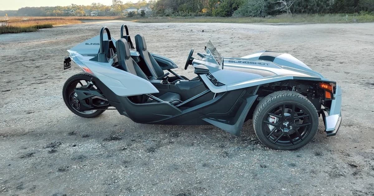 Three-wheeled open-top roadster on sandy beach terrain, coastal touring