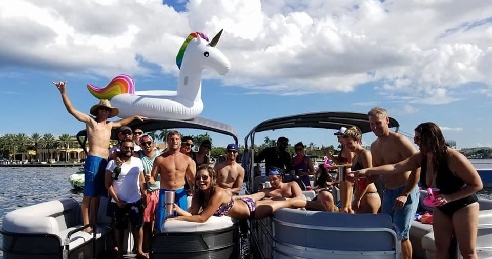 Friends partying on boat with giant unicorn float, daytime fun