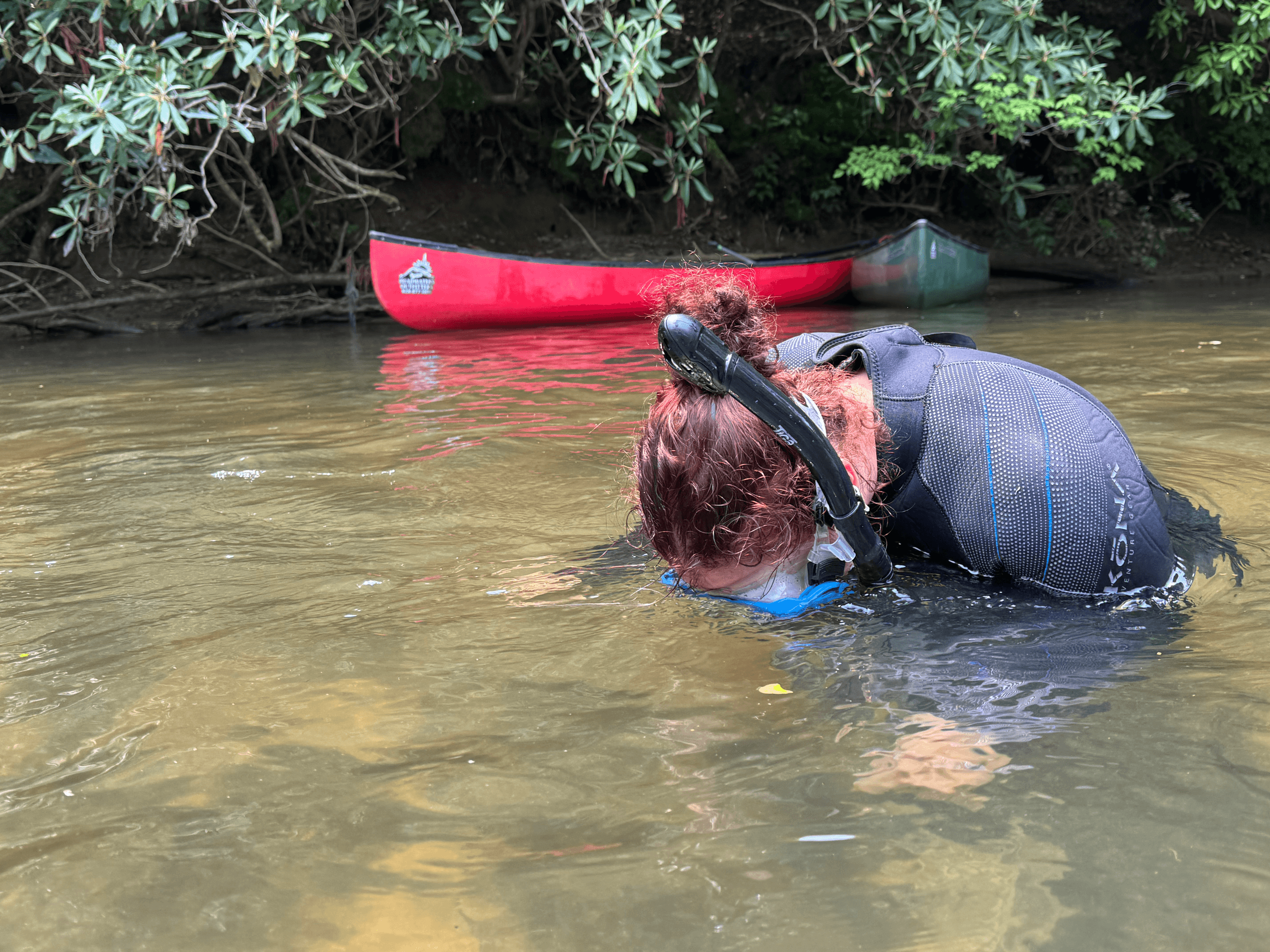 Adult river snorkeling near canoe in shallow creek, eco tour