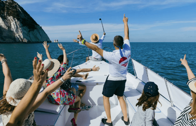 Group cheering on bow of boat with cliffs in background, party cruise