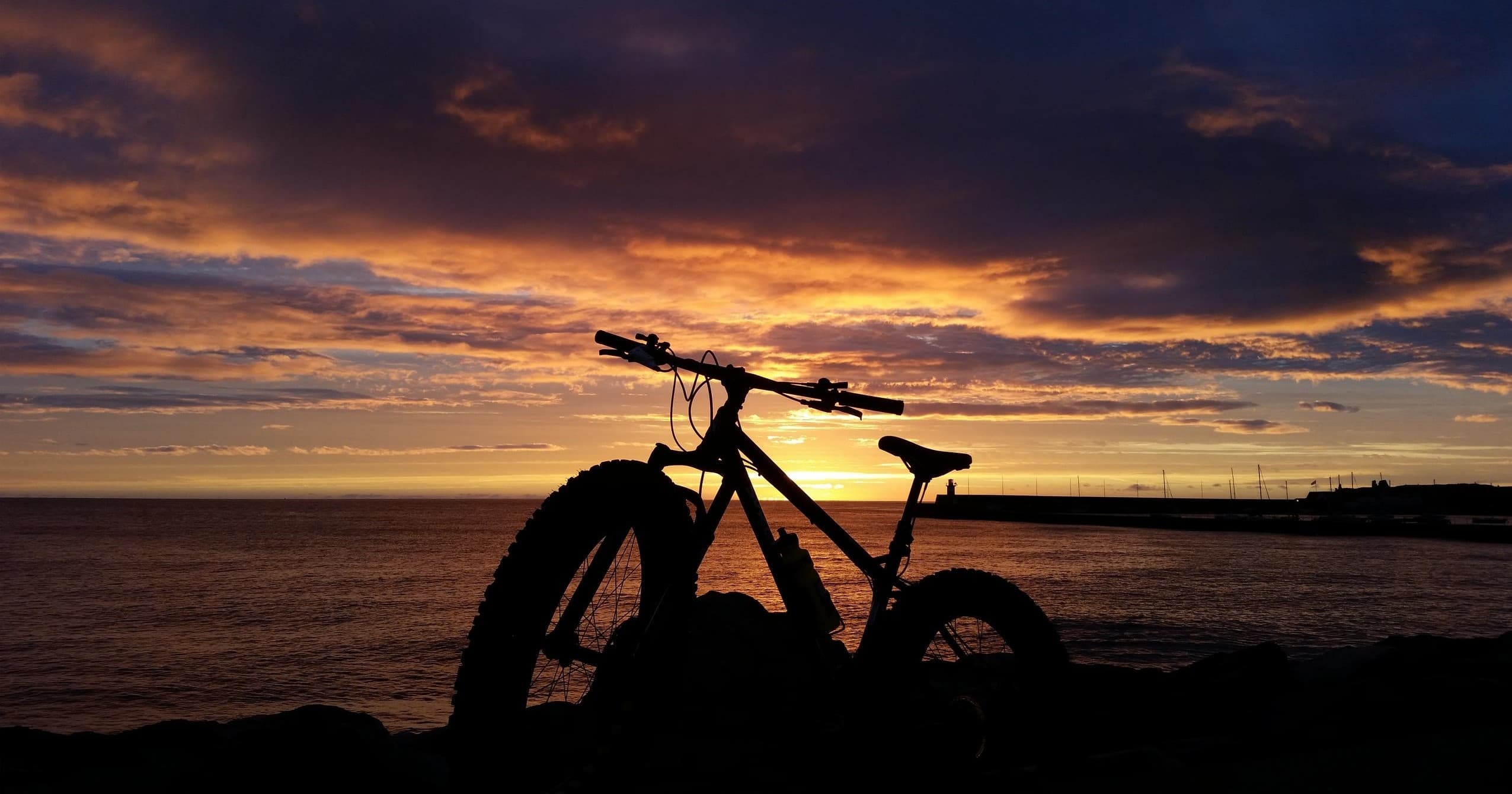 Fatbike silhouette at coastal sunset on rocky shoreline