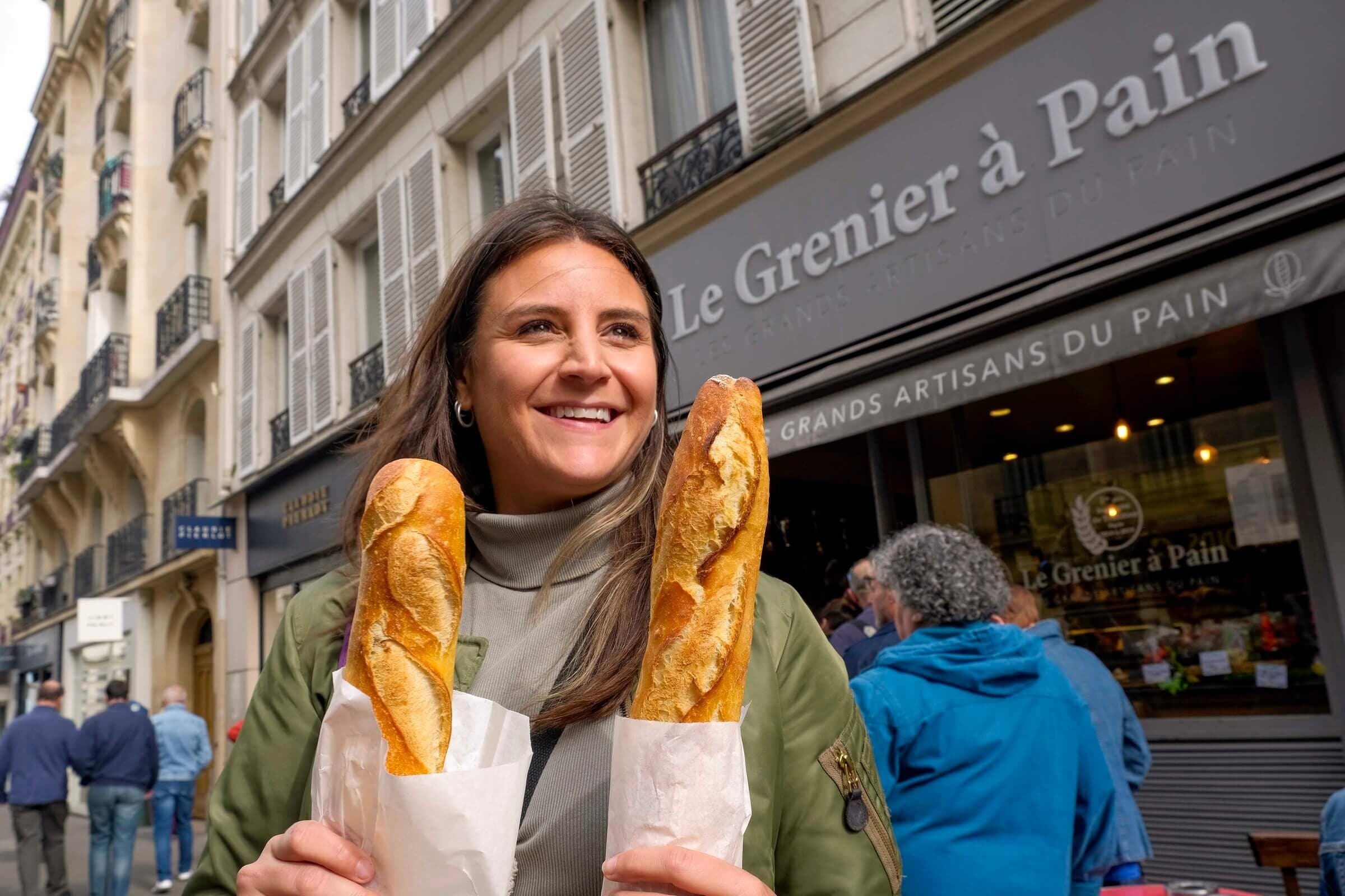Smiling visitor holding two baguettes outside Paris bakery on street