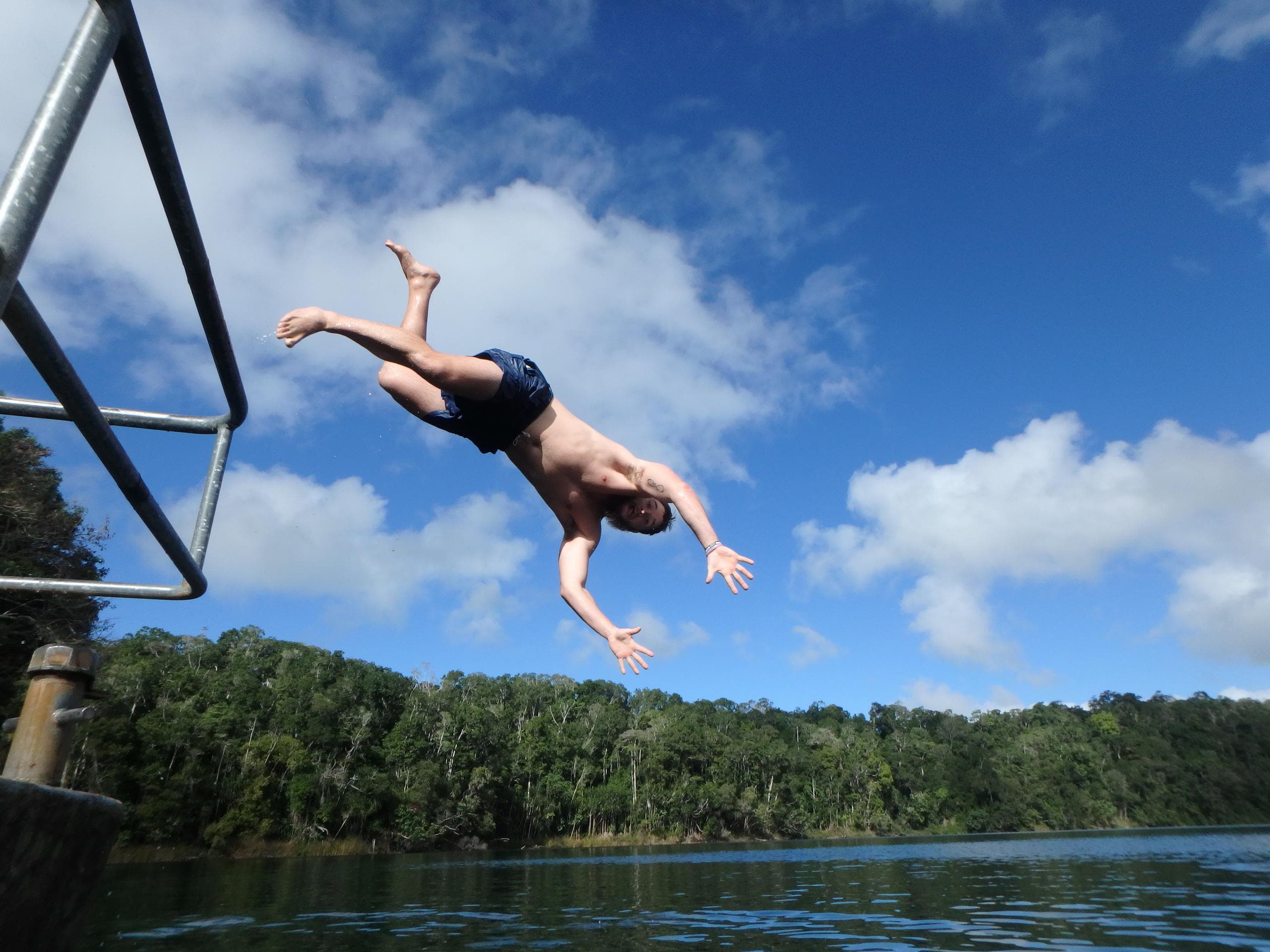 Diver midair leaping from platform into jungle lake waters