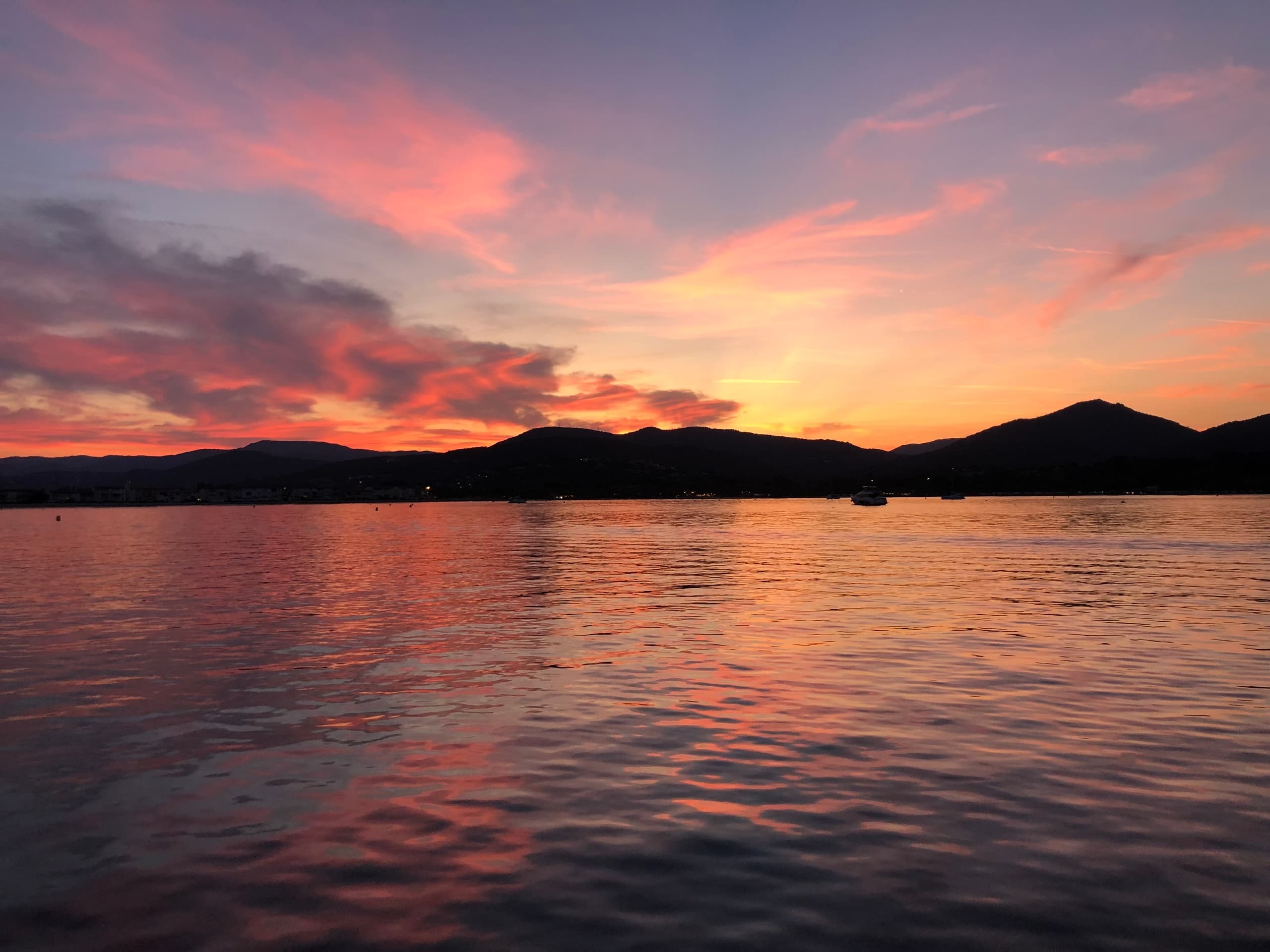 Sunset over calm sea with silhouetted island and reflective orange sky