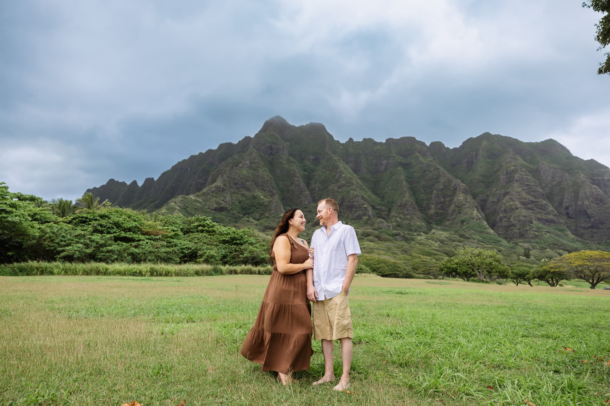 Couple standing in grassy field with dramatic mountain backdrop
