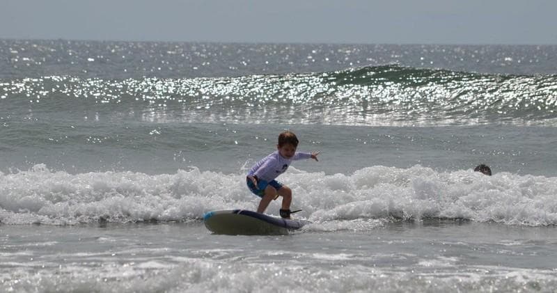 Young surfer riding small breaking waves on a sunny ocean beach
