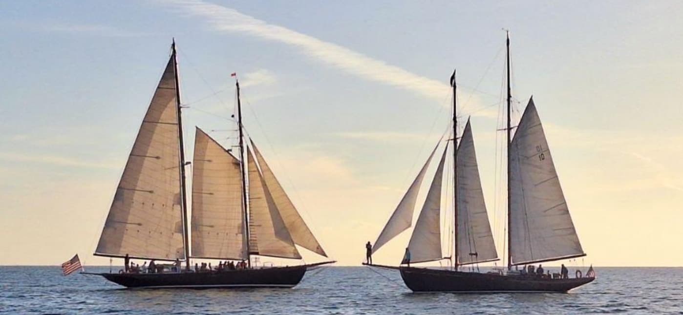Two tall sailing yachts racing across open sea at dusk