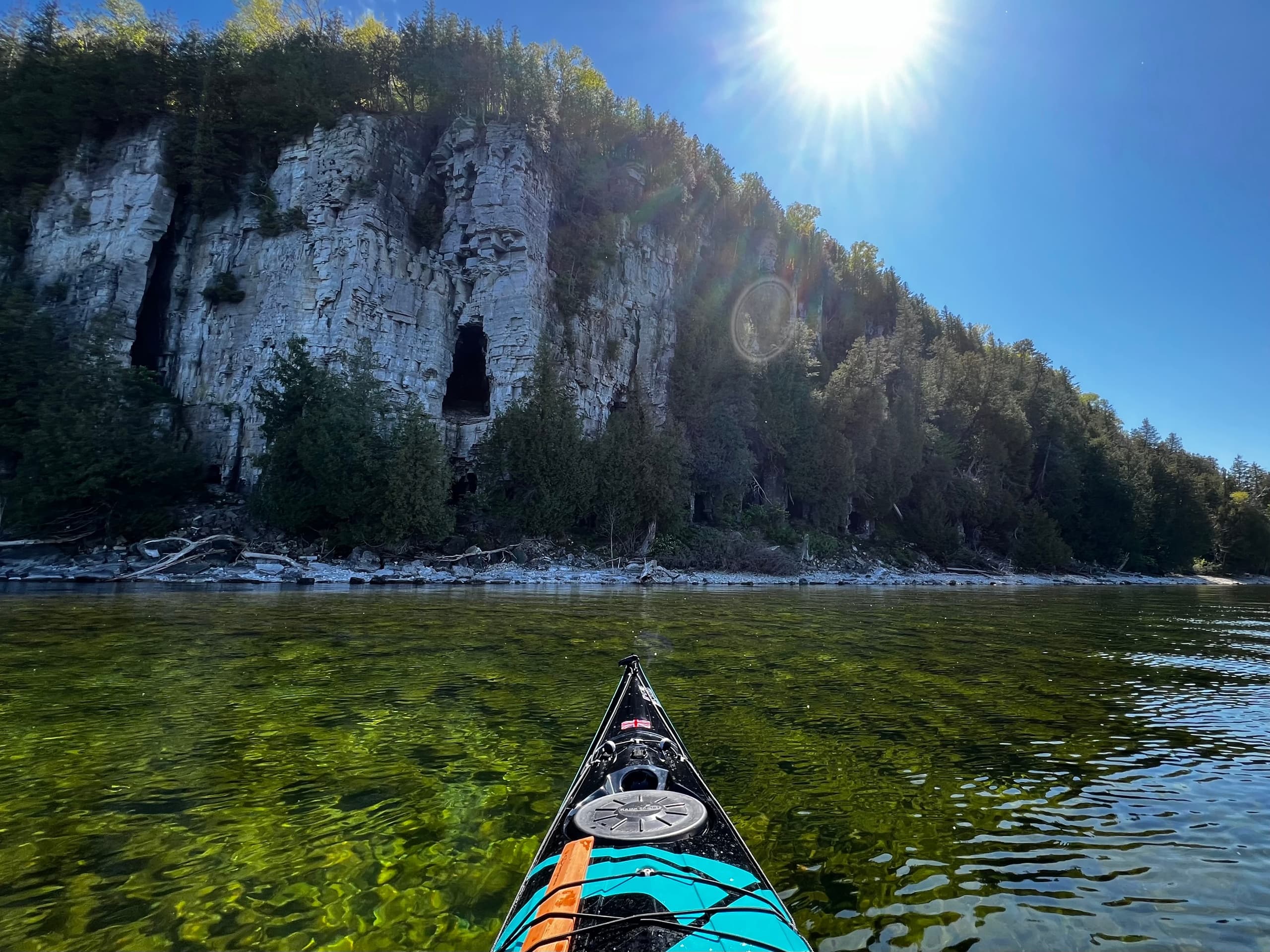 Kayak bow facing sunlit limestone cliffs over crystal clear water