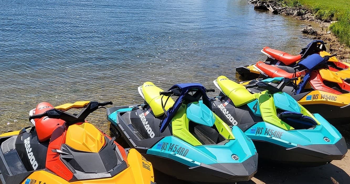 Colorful lined-up jet skis parked on rocky lakeshore, rental fleet