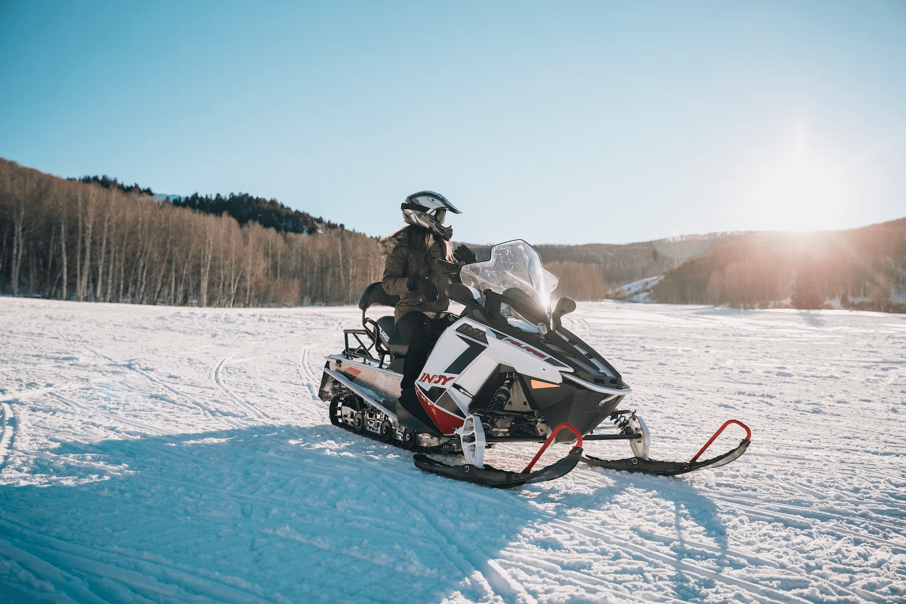 Rider snowmobiling across sunny alpine meadow with distant trees