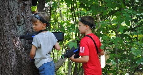 Kids playing outdoor laser tag in forest near trees, hiding