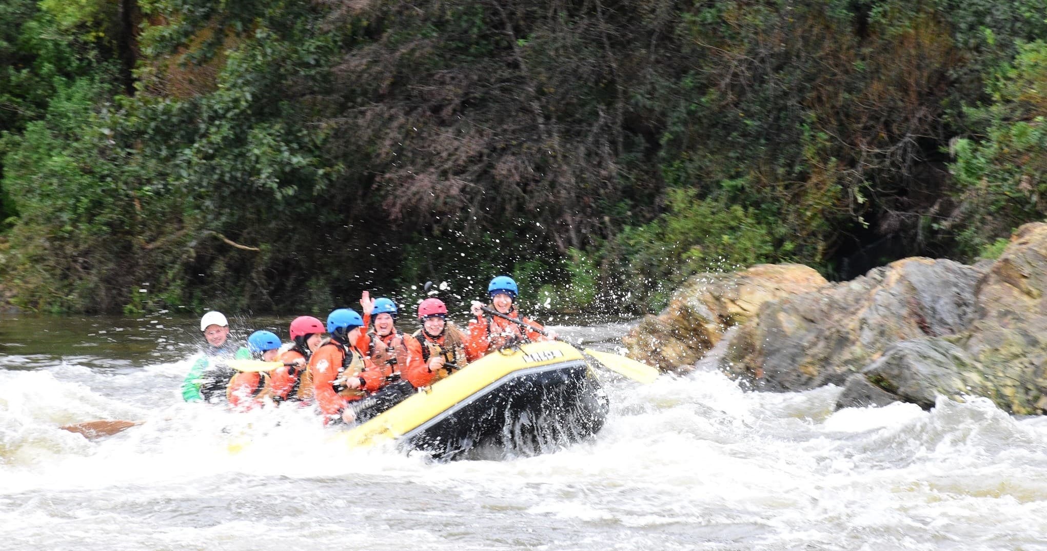 Raft cresting big rapid with spray on remote NZ river trip