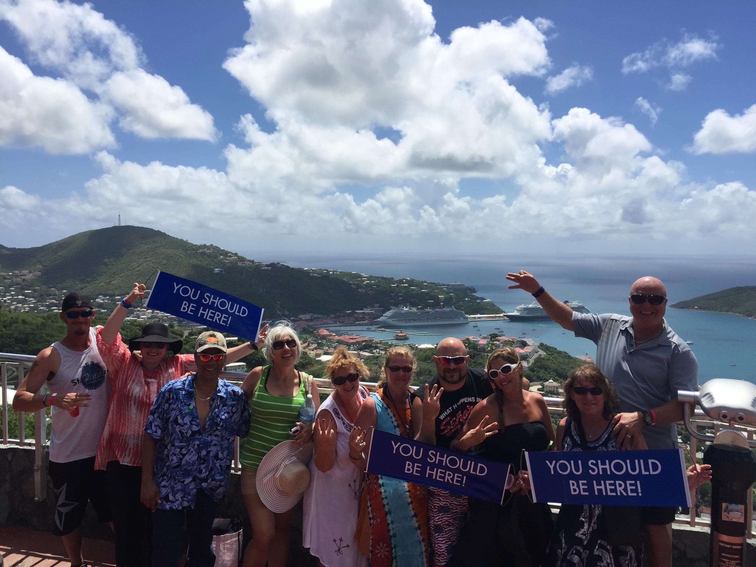 Group holding 'You Should Be Here' signs at island lookout