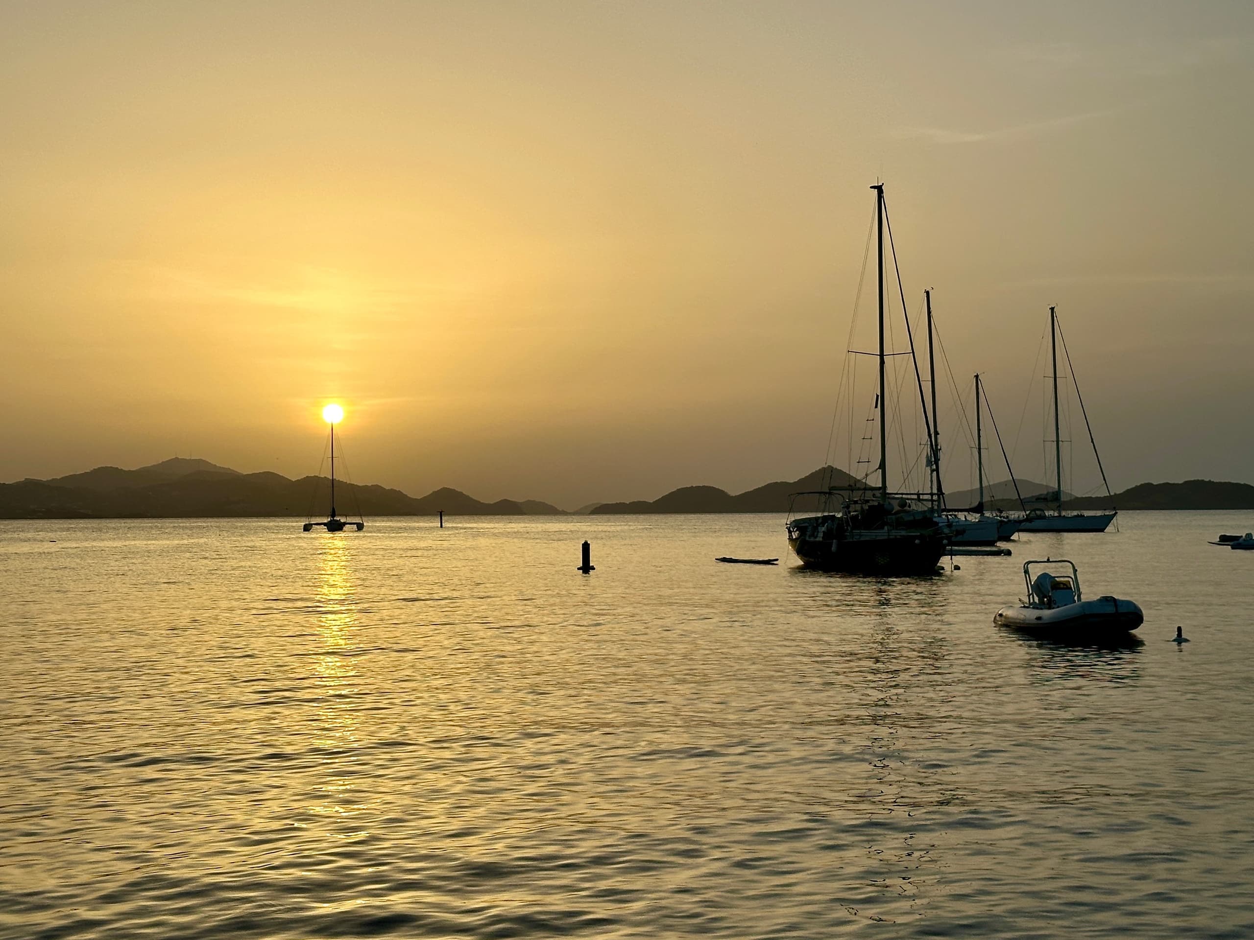 Sailboats moored at sunset over calm bay with golden sky