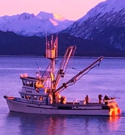 Commercial fishing trawler at sunset with crew near mountain coast