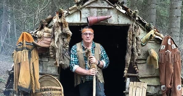 Guide standing at rustic wilderness cabin with furs in forest