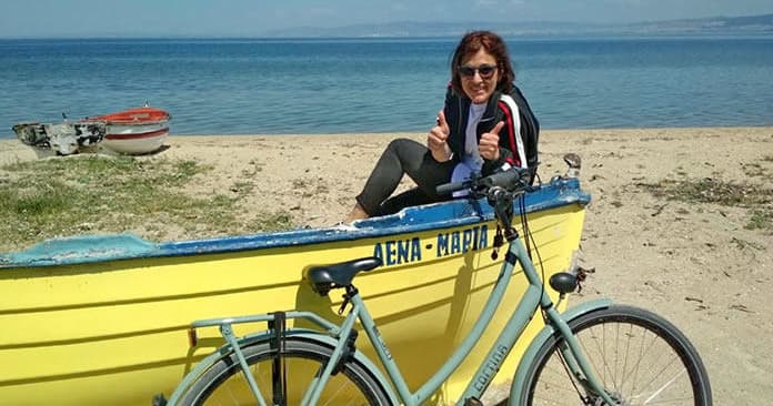 Woman posing on yellow boat with bicycle on sandy beach