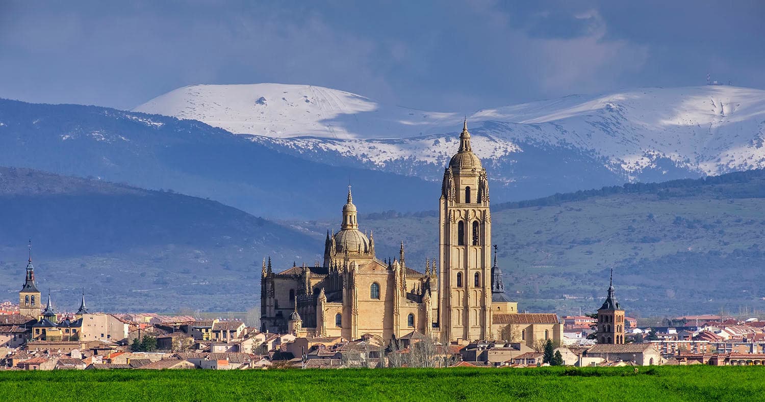 Distant Segovia cathedral with mountain backdrop and green foreground