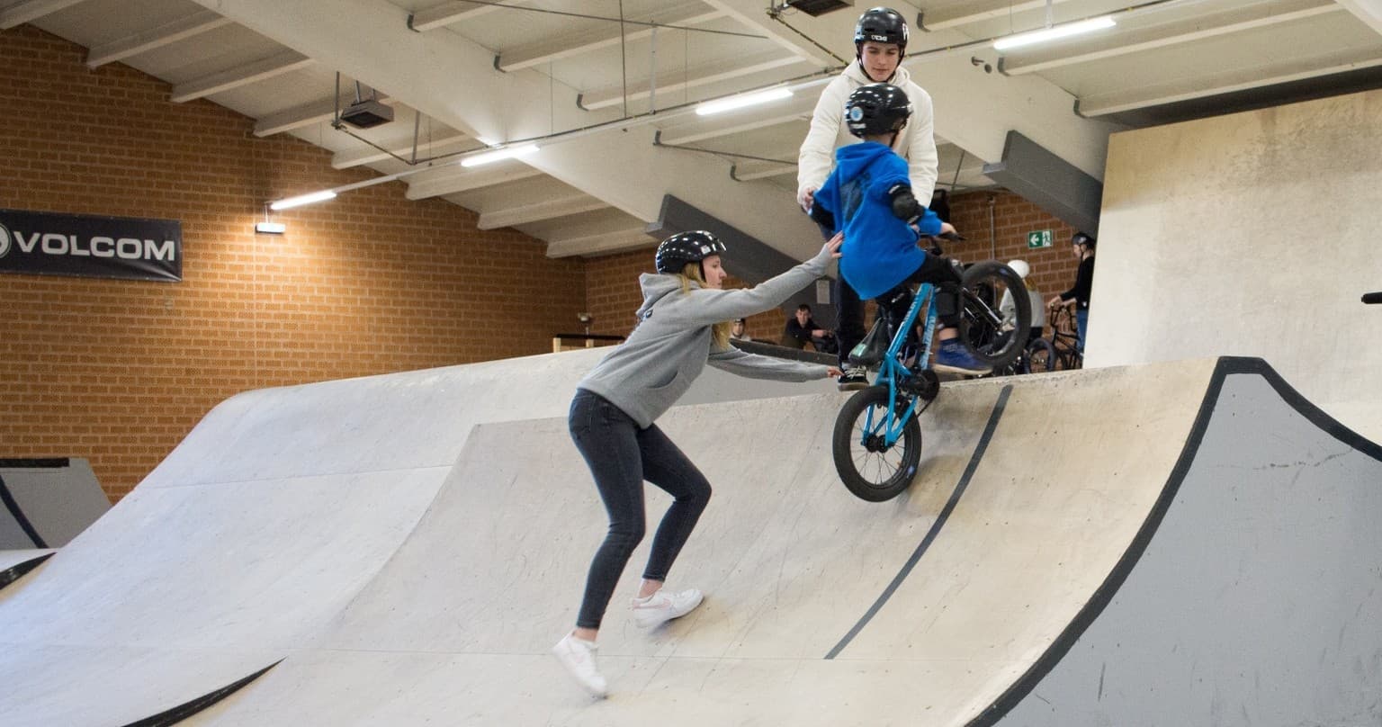 Instructor assisting BMX rider on curved ramp inside skatehalle Oldenburg