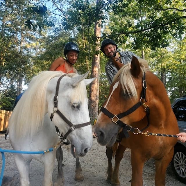 Close-up of two horses with riders at wooded farm corral