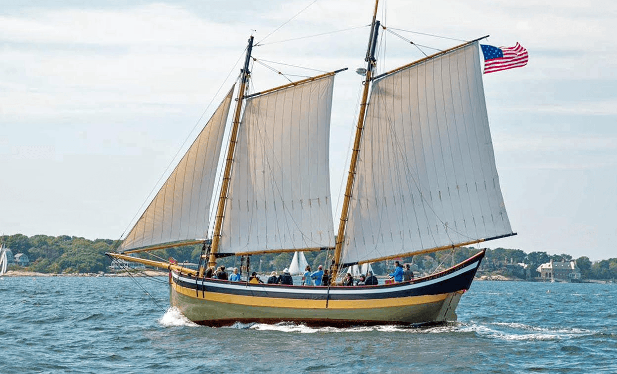 Schooner under full sail on blue harbor waters with American flag