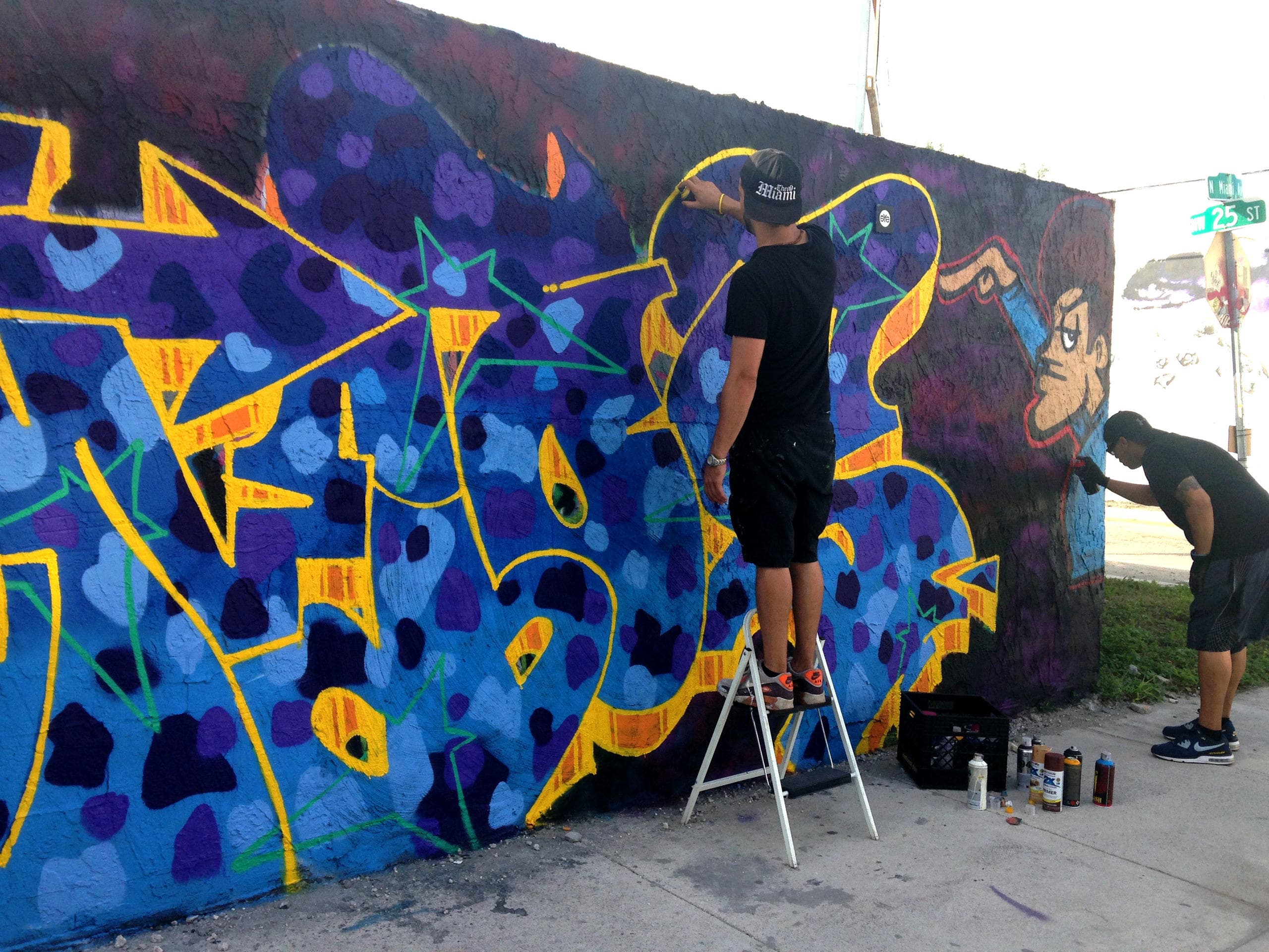Artist painting vibrant graffiti mural on outdoor Wynwood wall
