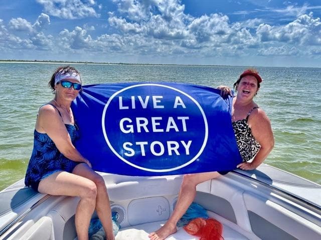 Two people boating on coastal waters holding a blue banner
