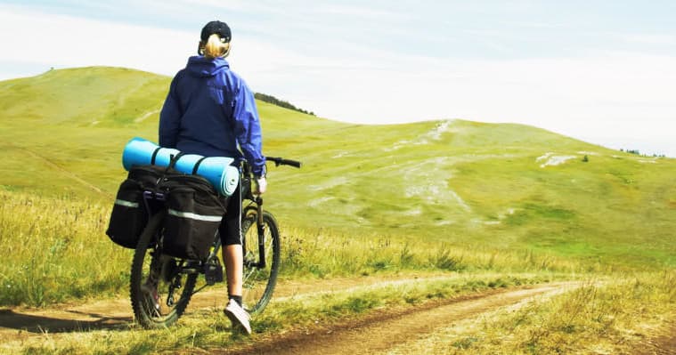 Solo cyclist with panniers biking across grassy rolling hills