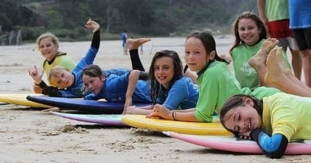Group of kids with surfboards smiling on sandy beach surf camp