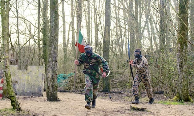Players running through forest paintball course in camouflage