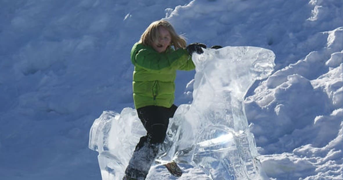 Child climbing clear ice sculpture on snowy hillside