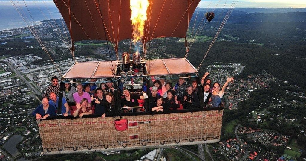 Hot air balloon basket with passengers soaring above landscape