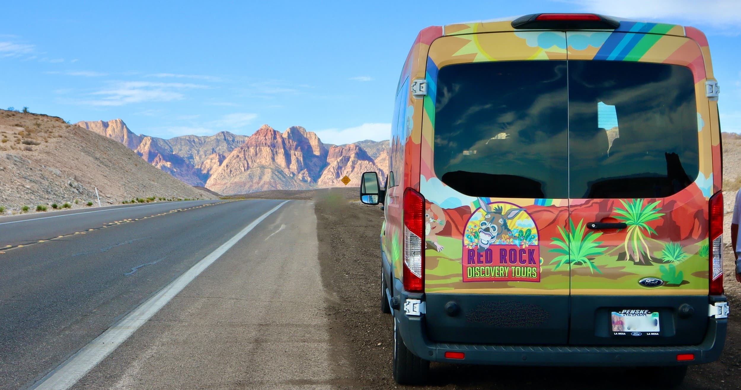 Tour van parked on scenic highway near red rock mountains