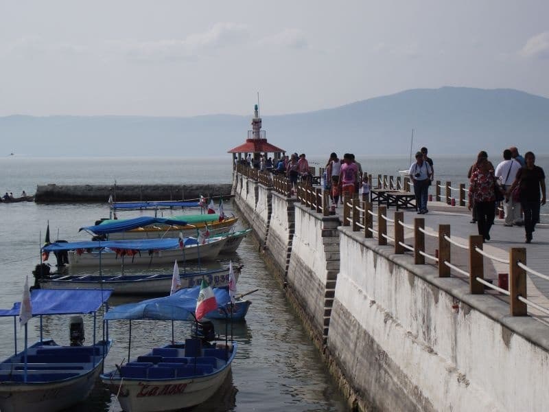 Scenic lakeside pier with fishing boats and pedestrians, coastal Jalisco
