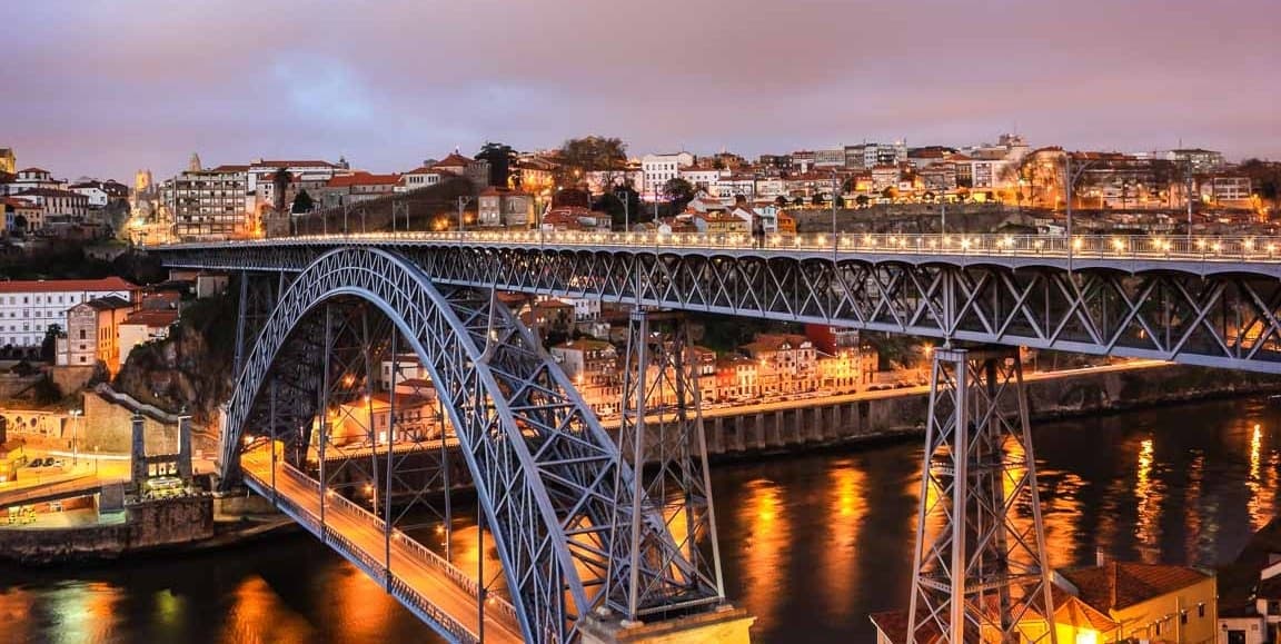 Historic steel city bridge lit at dusk over waterfront